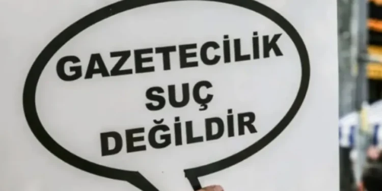 Gazetecilik suç değildir" yazılı bir döviz tutan el.