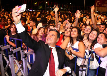 Takım elbiseli bir adam kalabalık bir grupla selfie çekiyor.