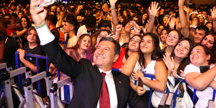 Takım elbiseli bir adam kalabalık bir grupla selfie çekiyor.