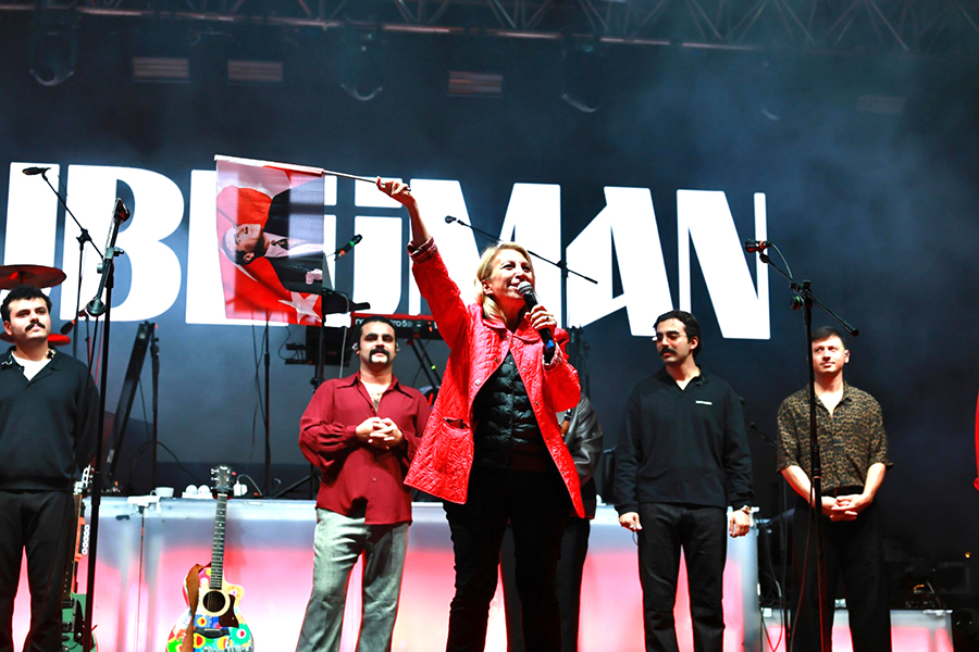 Konser sahnesinde elinde Atatürk bayrağı tutan kırmızı ceketli kadın.