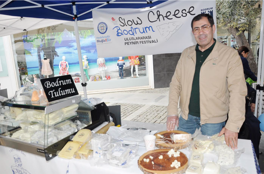 Slow Cheese Bodrum festivalinde peynir sergileyen gülen bir adam.