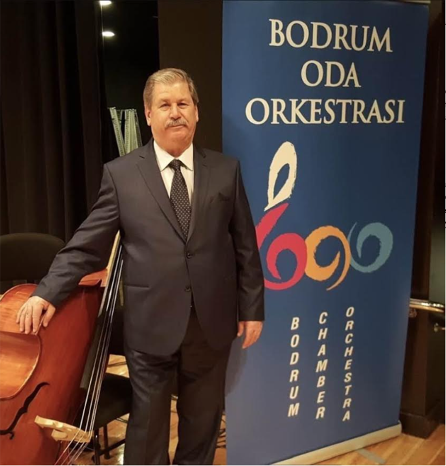 Takım elbiseli bir adam, çello ve orkestra afişi yanında.