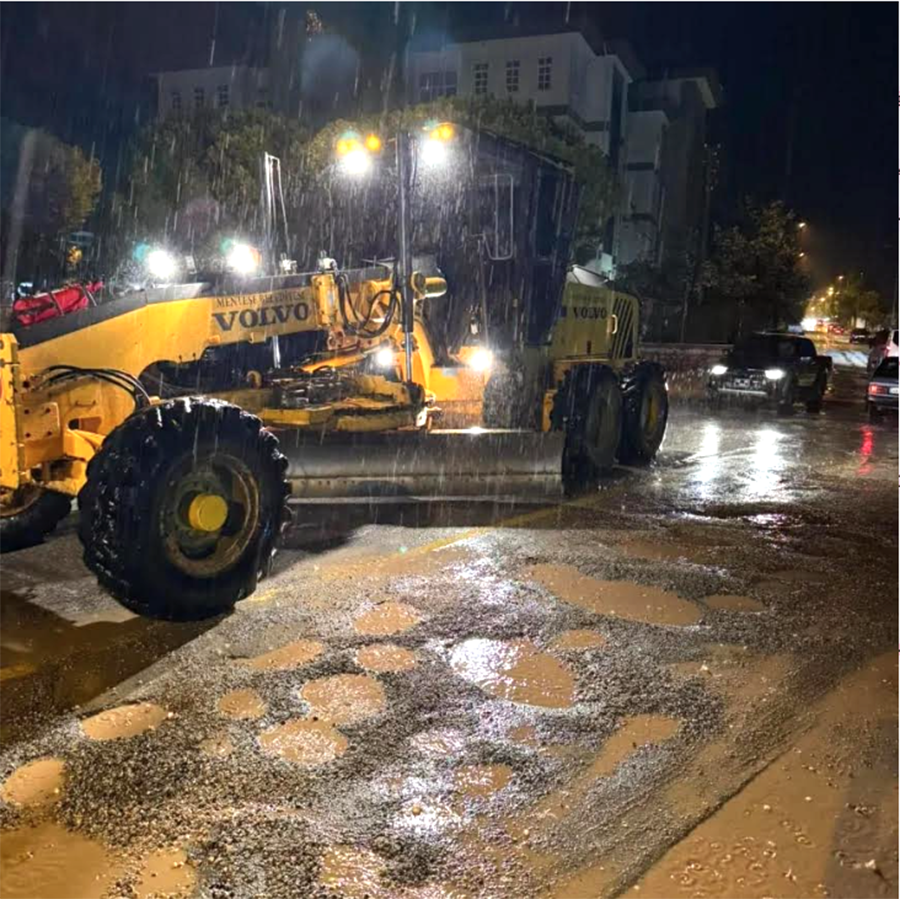 Gece yağmurda çukurlu yolda çalışan Volvo greyder iş makinesi.