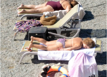 Çakıllı plajda şezlonglarda güneşlenen iki kadın.