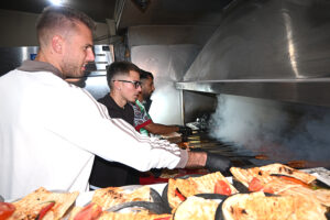Ocakbaşı ızgarasında kebap pişiren adamlar ve ön planda pideler.