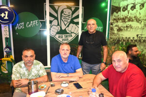 Asi Cafe'de Bodrumspor logolu bir duvar önünde oturan dört adam.