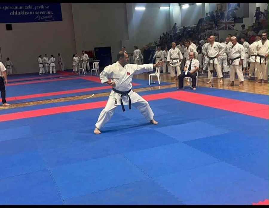 Mavi mat üzerinde karate pozu veren siyah kuşaklı sporcu.