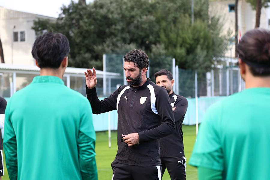 Antrenman sahasında futbolculara talimat veren sakallı bir teknik direktör.