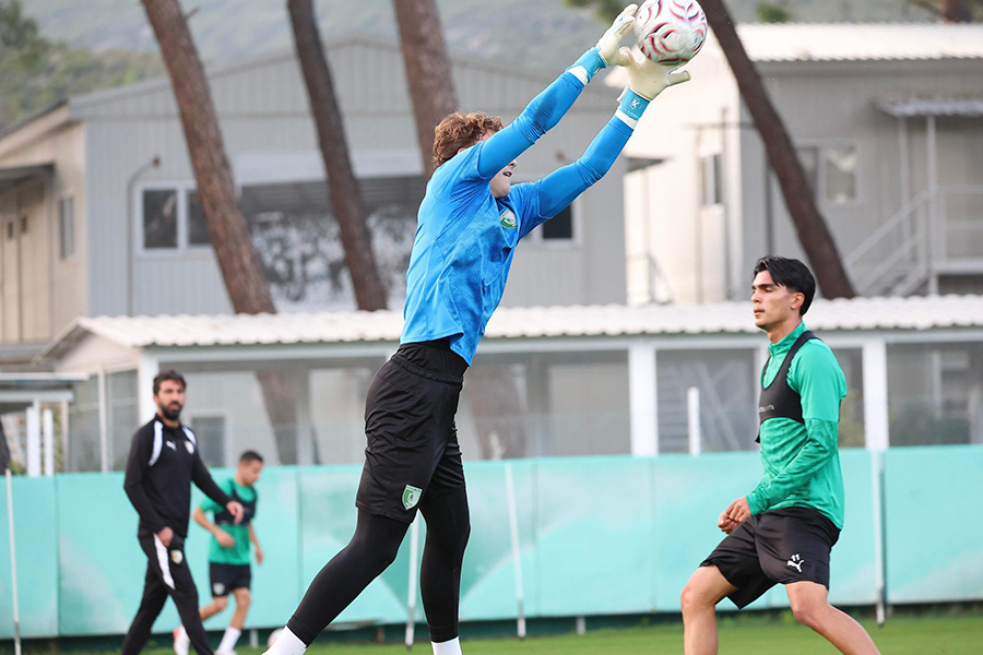 Antrenmanda topu yakalamaya çalışan genç bir futbol kalecisi.